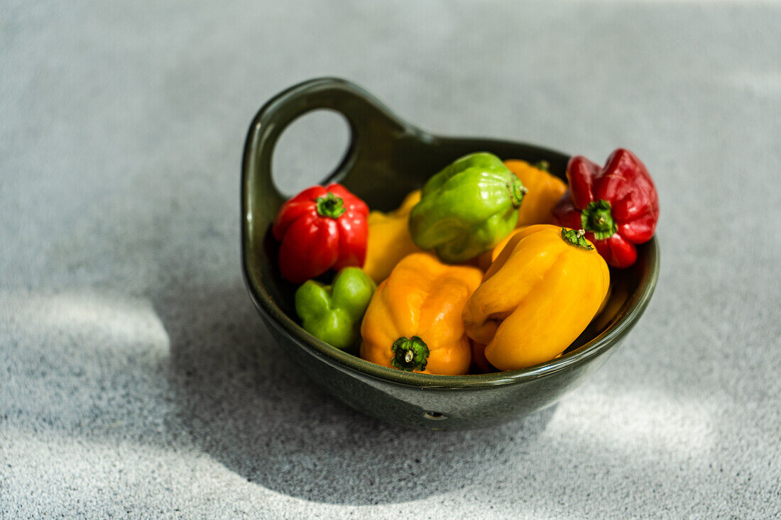 Top view of different colored peppers placed in a round black ceramic bowl on a concrete background