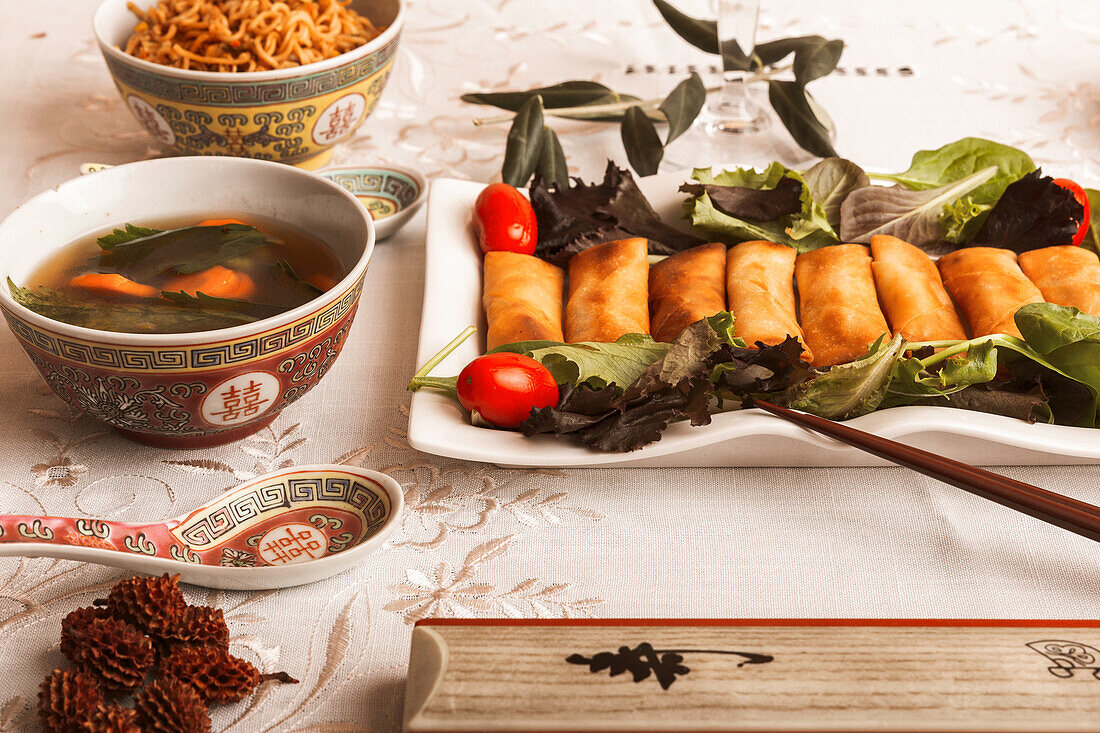 Asiatisches Essgeschirr mit vietnamesischen Brötchen auf einem Teller, einer Schale mit Suppe, Reis und Stäbchen