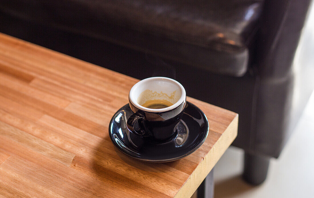 Hohe Winkel der Tasse heißen aromatischen Espresso auf schwarze Untertasse über Holztisch von Sofa im Wohnzimmer bei Tageslicht platziert