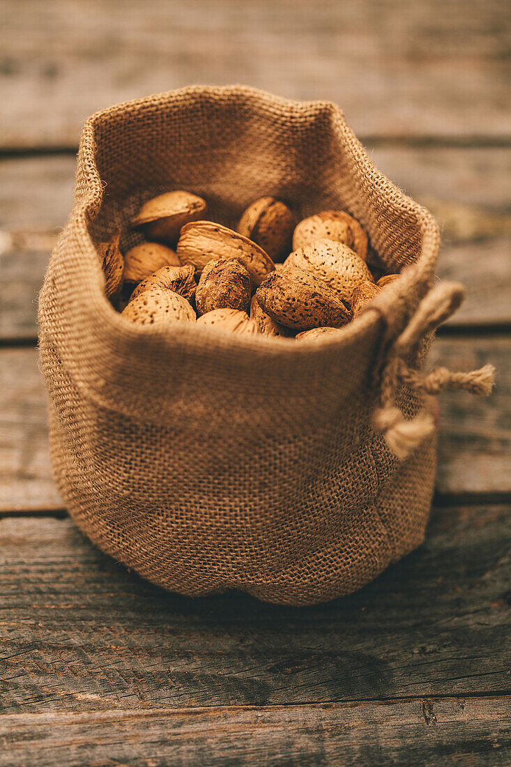 A soft-focus view of almonds in an open burlap pouch, gently resting on a wooden surface
