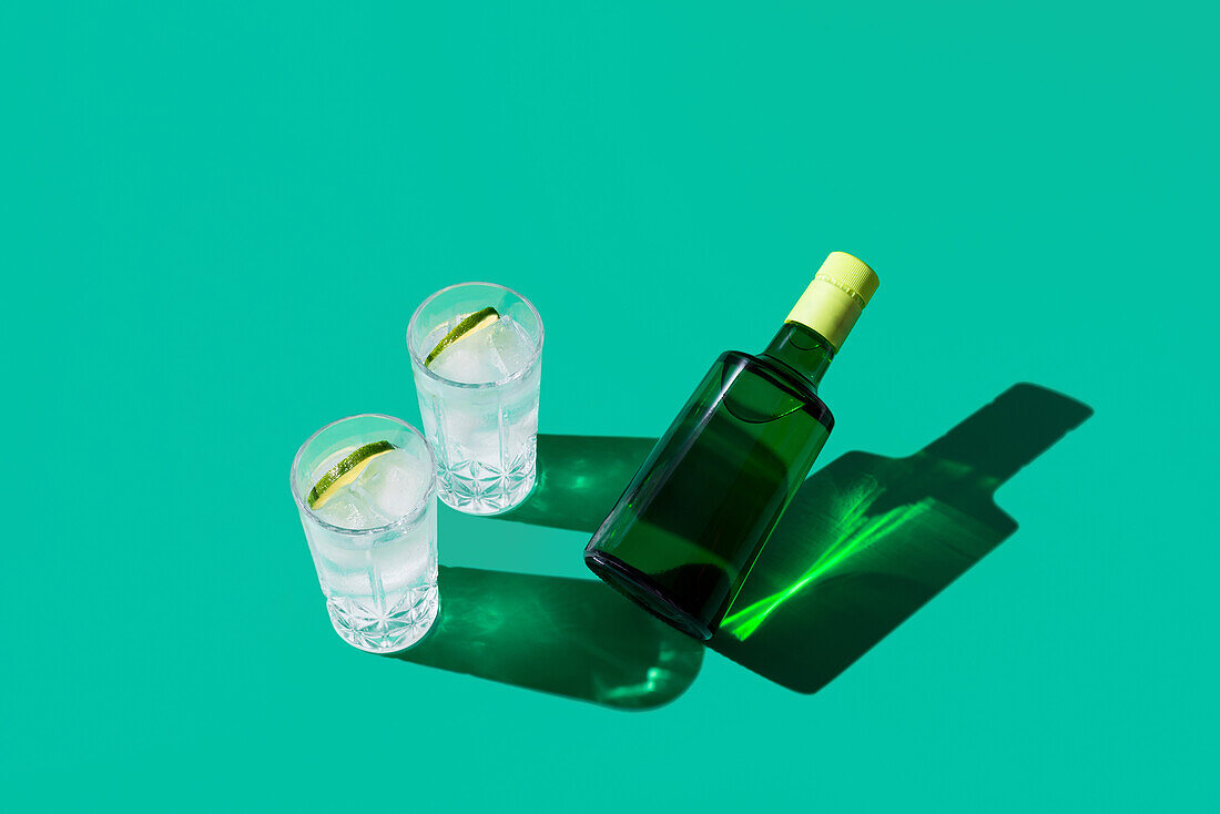 A stylish gin tonic cocktail in a glass with a slice of lime, showcased on a green backdrop with sharp shadows.