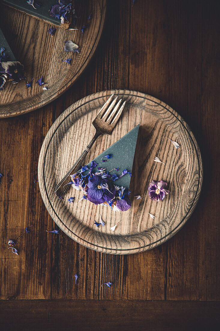Draufsicht auf eine Tortenscheibe aus blauer Spirulina und mit Blumen dekoriert auf einem Holztisch