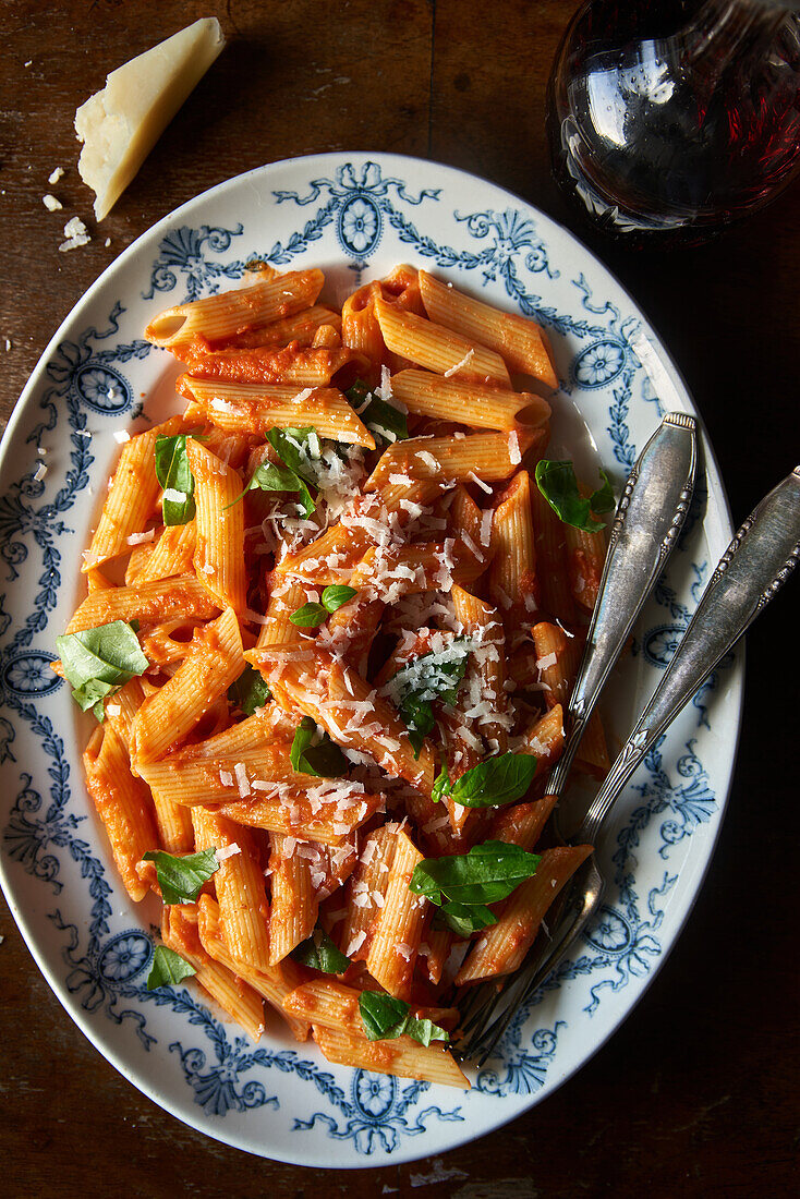 A rustic plate of penne pasta covered in rich tomato sauce, sprinkled with parmesan and fresh basil leaves, illuminated by natural light