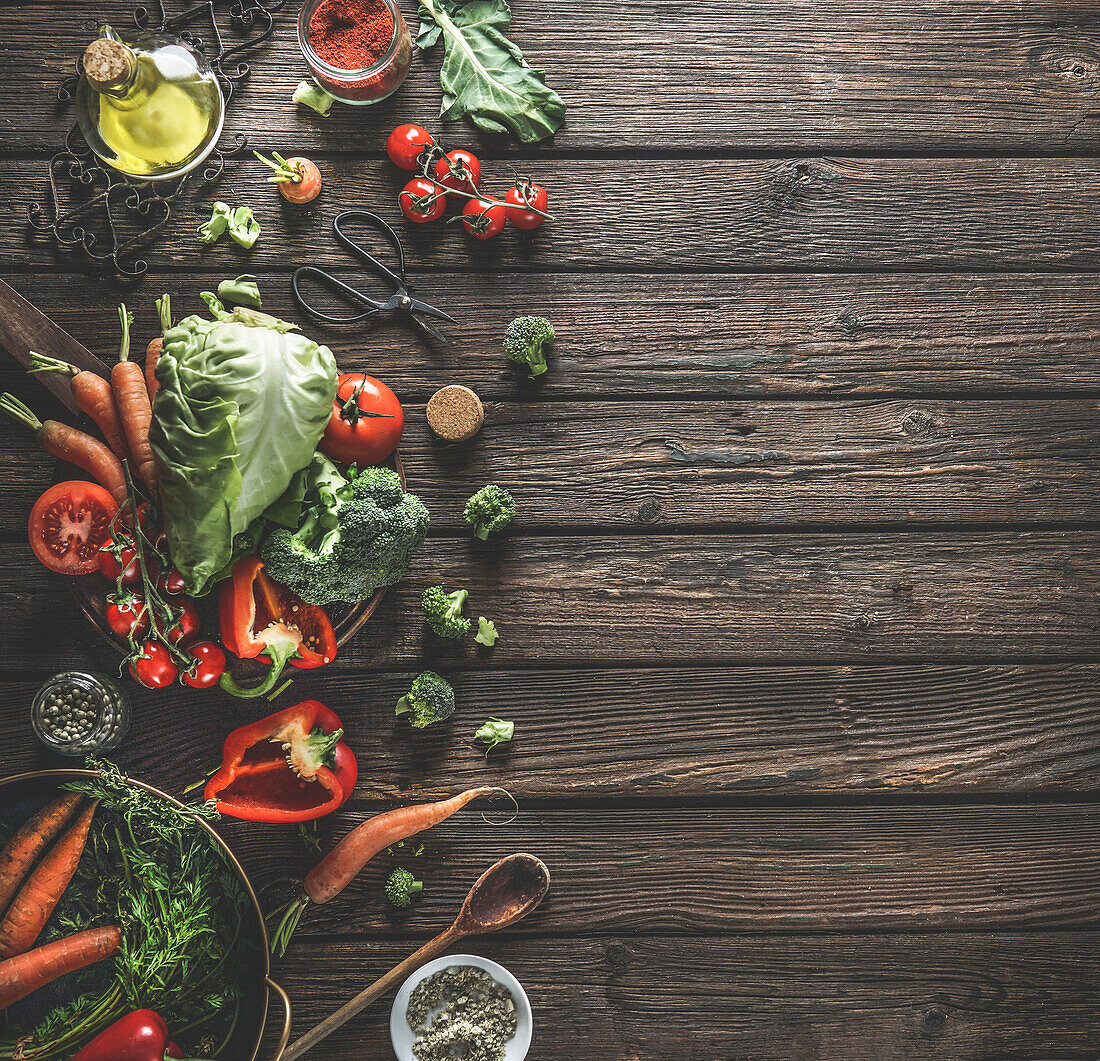 Food background with organic vegetables, healthy ingredients and kitchen utensils on dark rustic wooden table. Top view. Copy space.