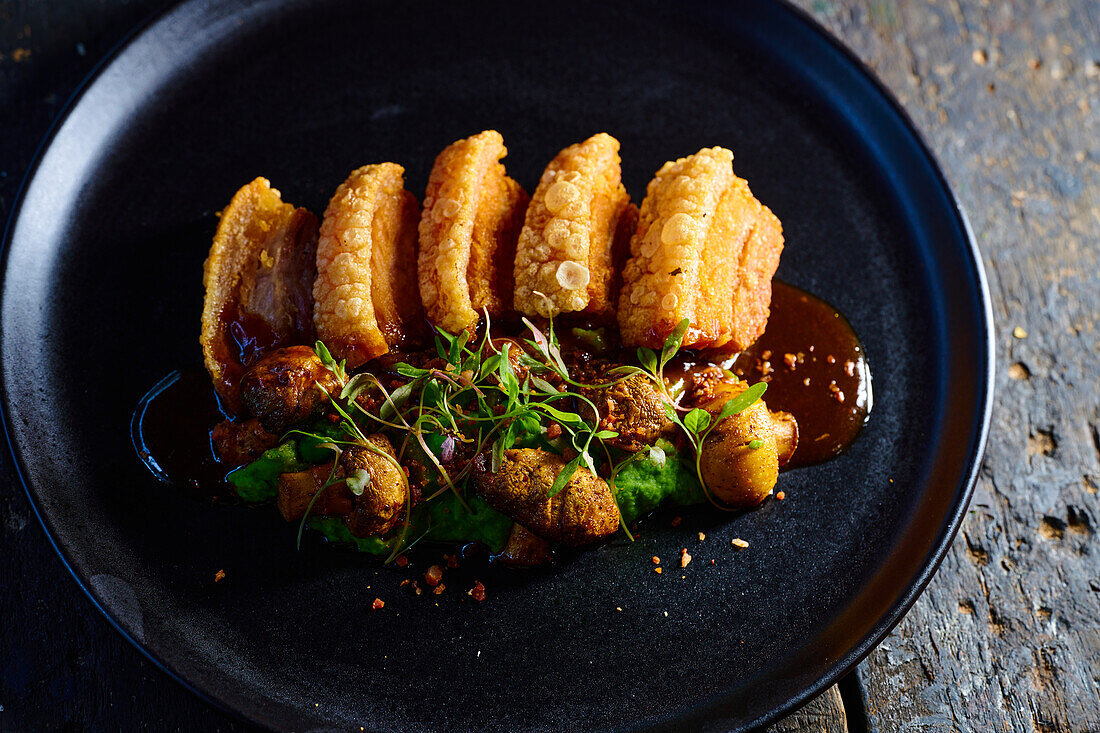 Draufsicht auf appetitliches, knusprig paniertes Fleisch, garniert mit Soße, Pilzen und Kräutern, serviert auf einem schwarzen Teller