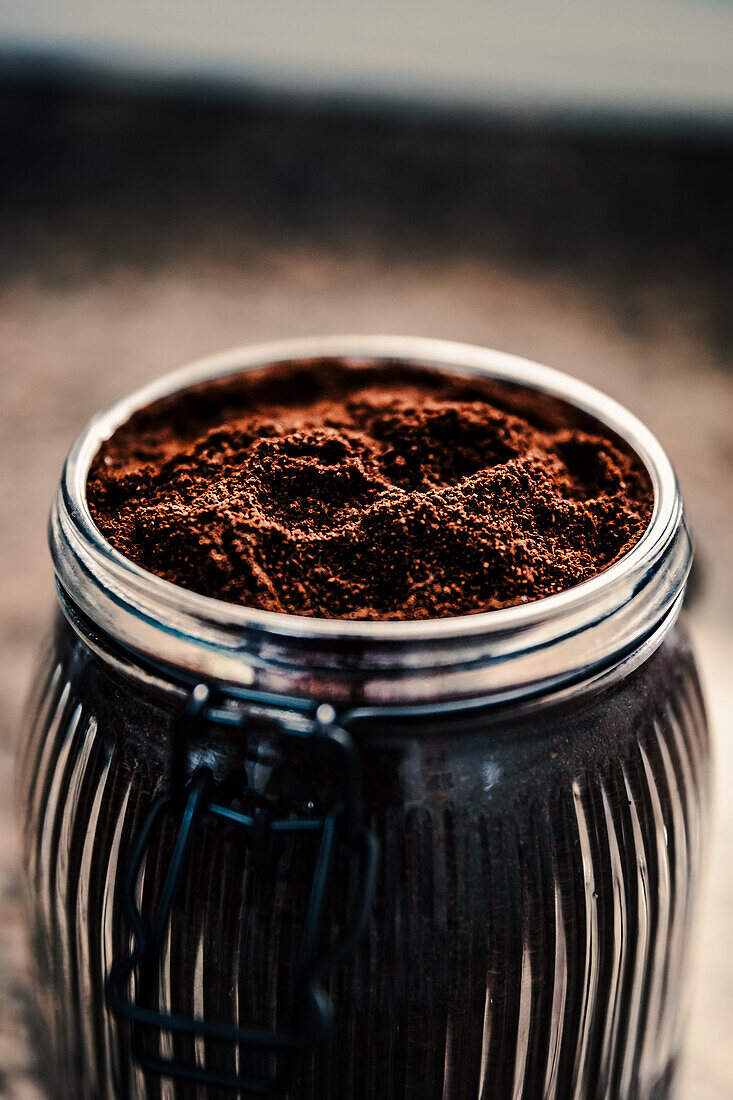 Draufsicht auf fein gemahlenen Kaffee in einem gerippten Glasgefäß, das seine reiche Textur und Tiefe hervorhebt, vor einem gesprenkelten Hintergrund