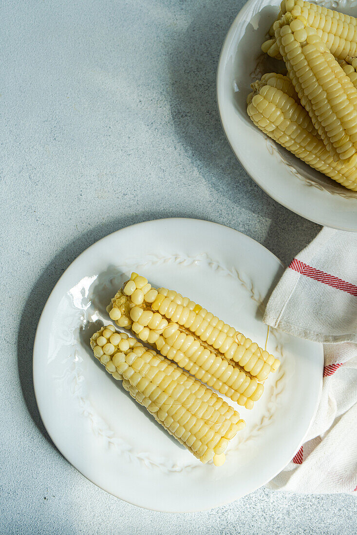Top view of ripe sweet corns served on plates near napkin on gray table