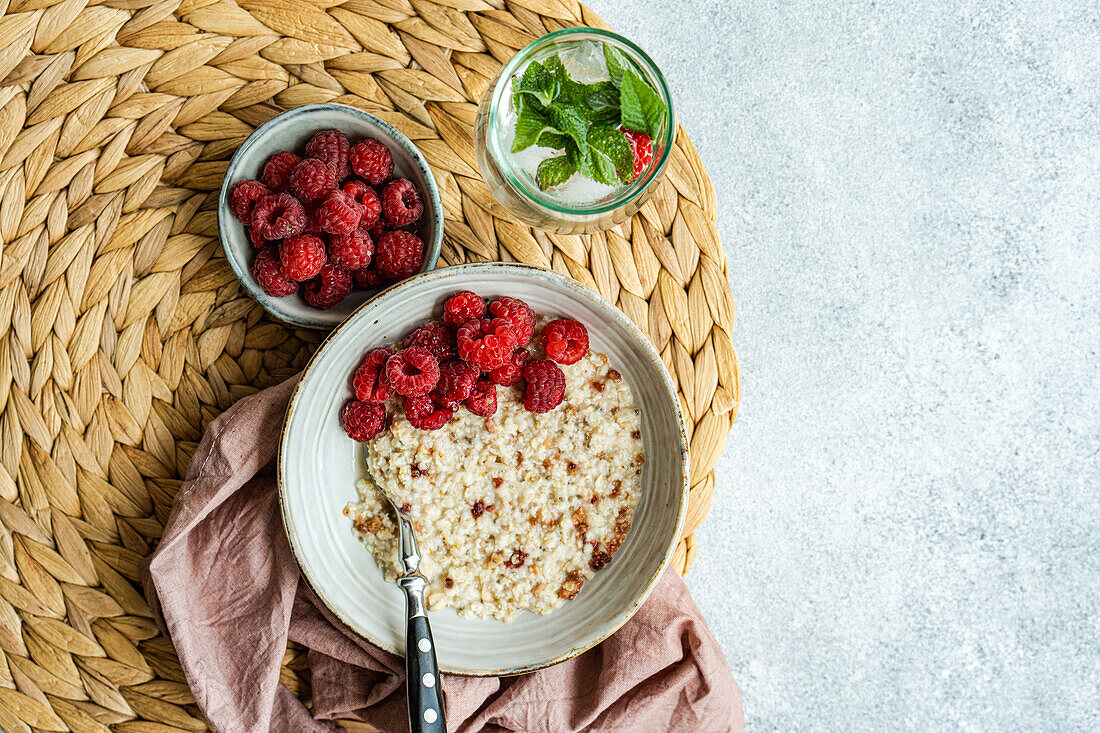 From above healthy breakfast with oatmeal with fresh organic raspberries and homemade lemonade on concrete table
