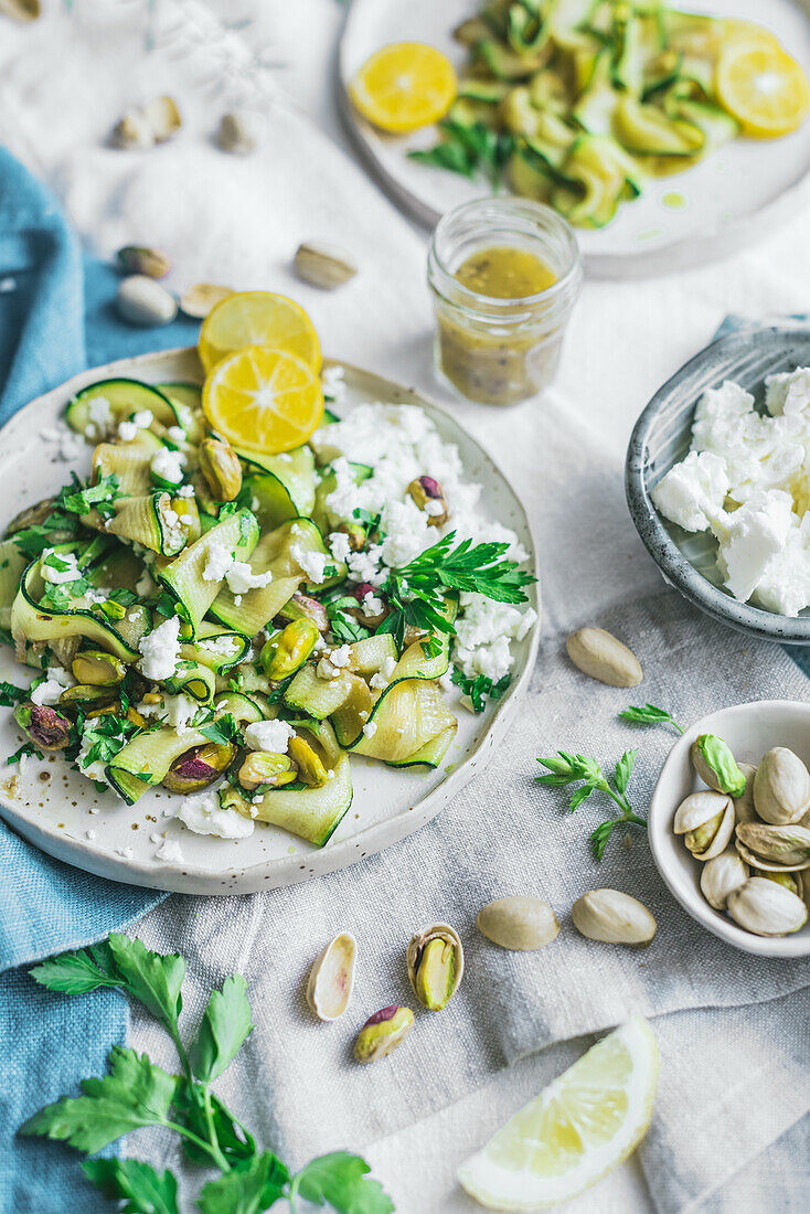 Top view of delicious healthy grilled courgette salad with feta cheese and pistachios served with slices on lemons and herbs on table