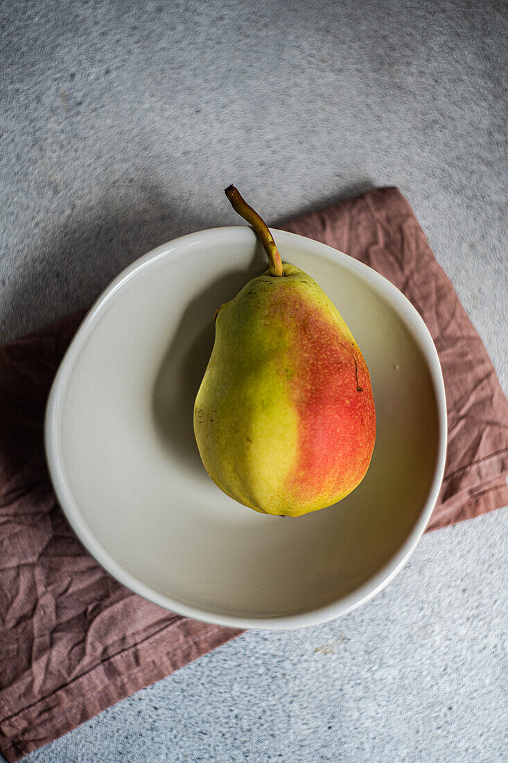 Draufsicht auf reife Bio-Birnenfrucht in Teller auf Serviette vor grauem, unscharfem Hintergrund