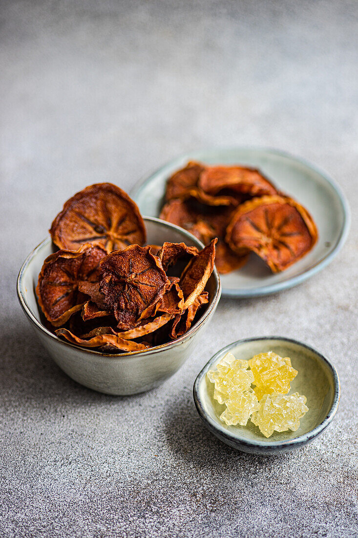 High angle of slices of dried apples and persimmon fruits served in ceramic bowls against blurred gray background