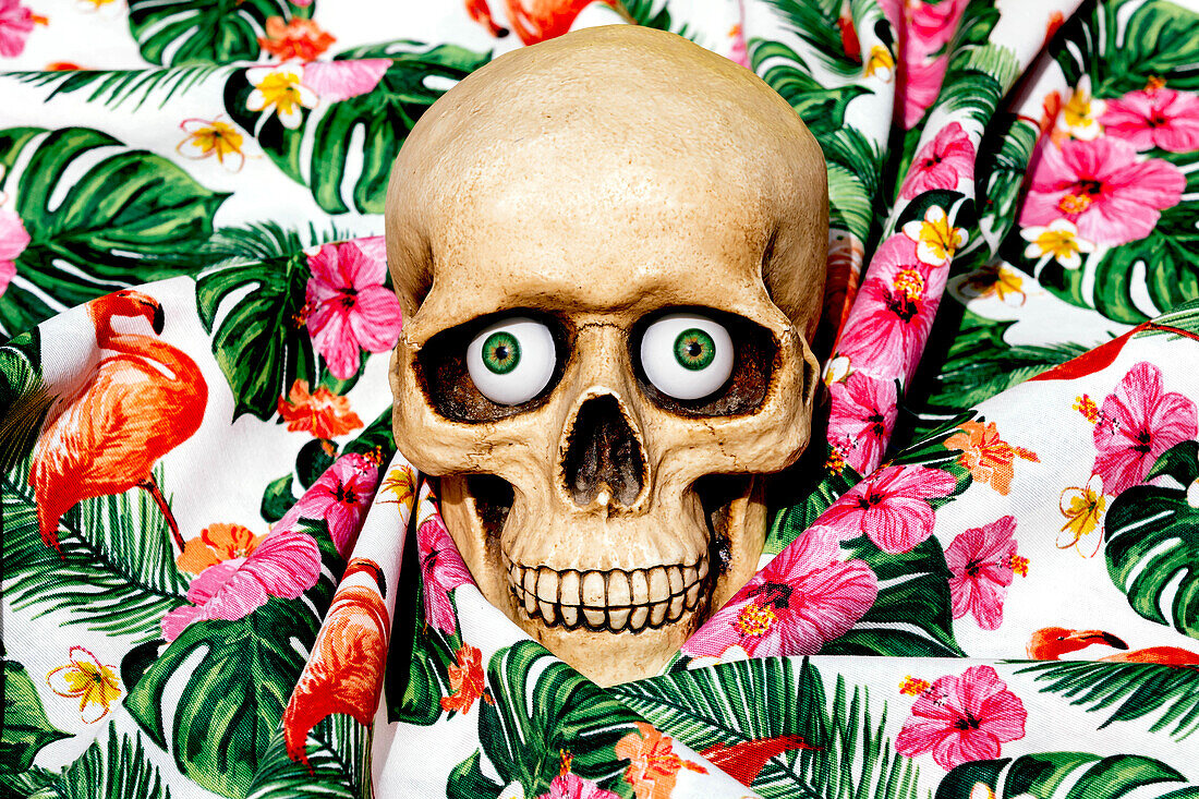 Spooky human skull looking at camera with green eyes while being placed on fabrics with drawn flowers