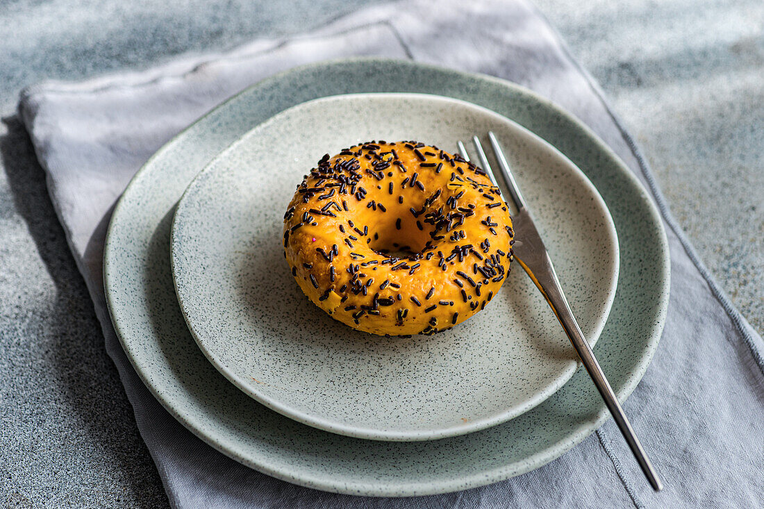 High angle of sweet banana donut placed on gray plate with fork on gray table