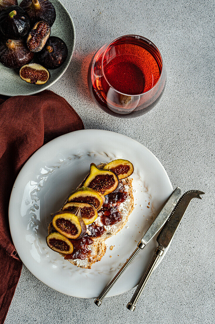 A gourmet toast topped with figs and jam, paired with a glass of red wine, presented on a white plate for a sophisticated snack.