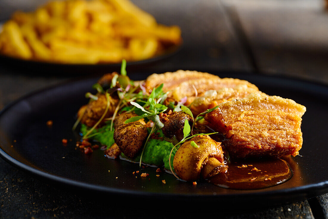 Delicious fried breaded meat garnished with mushrooms and herbs served on black plate near French Fries against blurred background