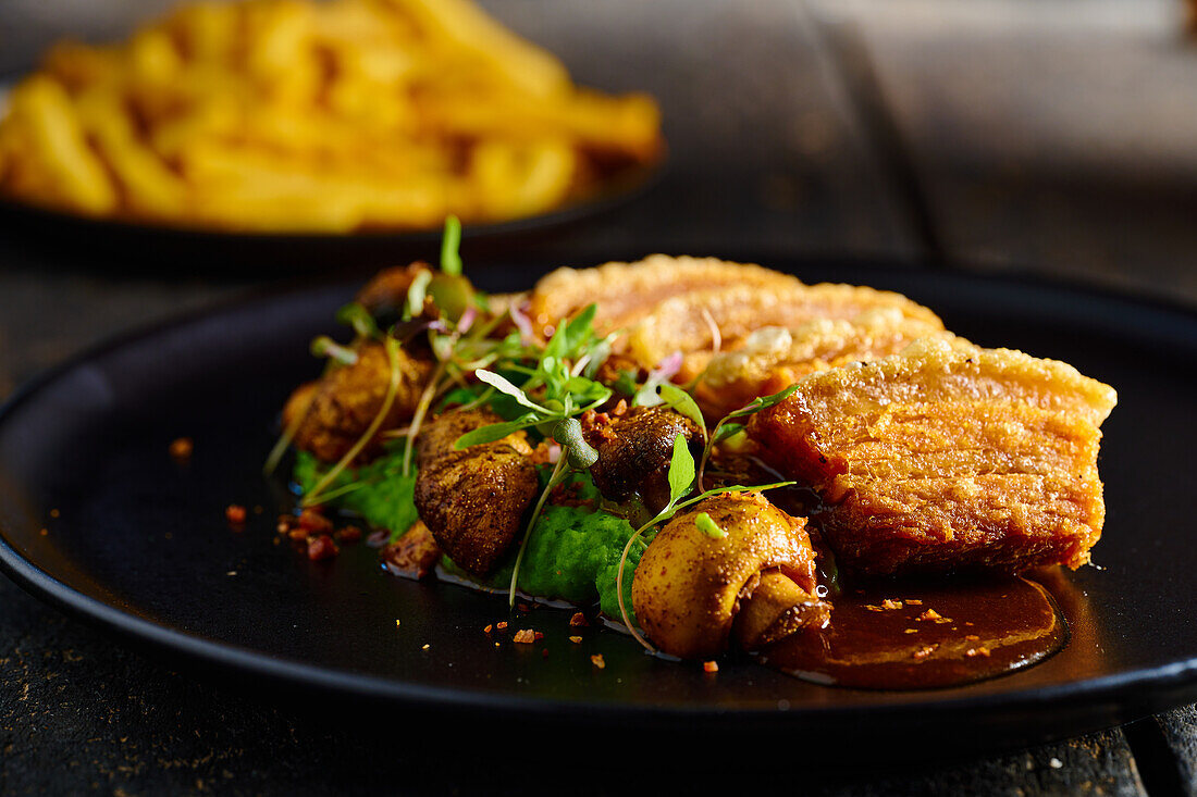 Köstlich gebratenes paniertes Fleisch, garniert mit Pilzen und Kräutern, serviert auf schwarzem Teller neben Pommes frites vor unscharfem Hintergrund
