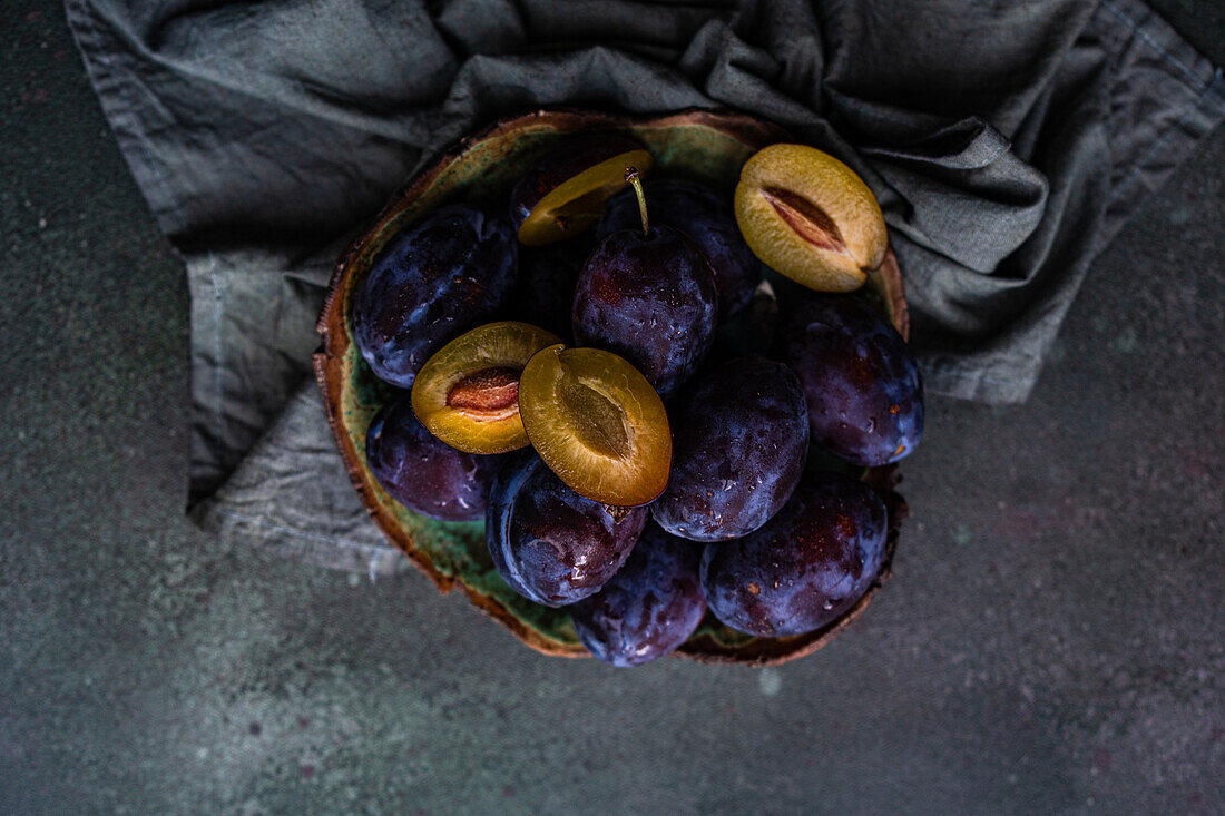 Top view of organic ripe plums served in marble bowl placed on napkin on gray surface