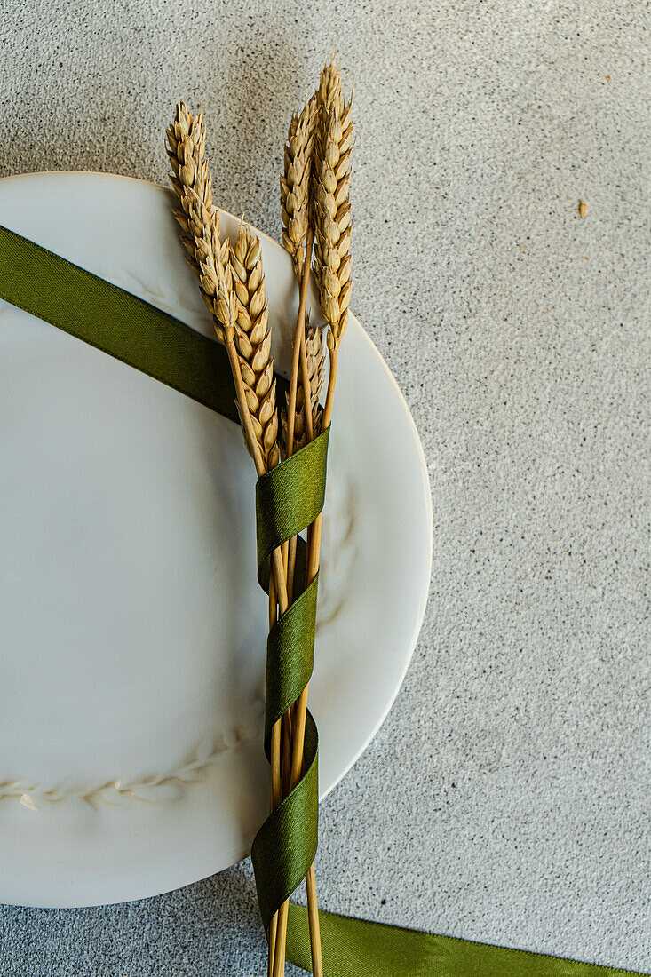 Draufsicht auf einen Strauß Weizenähren mit grünem Band auf einem Teller auf einem grauen Tisch