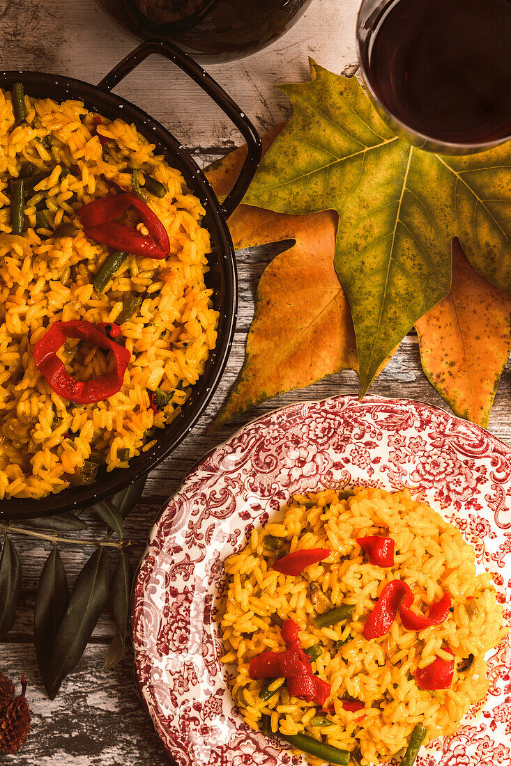 Ein vertikales Bild, das ein herzhaftes herbstliches Reisgericht zeigt, das in einer rustikalen Küche serviert wird, umgeben von bunten Herbstblättern