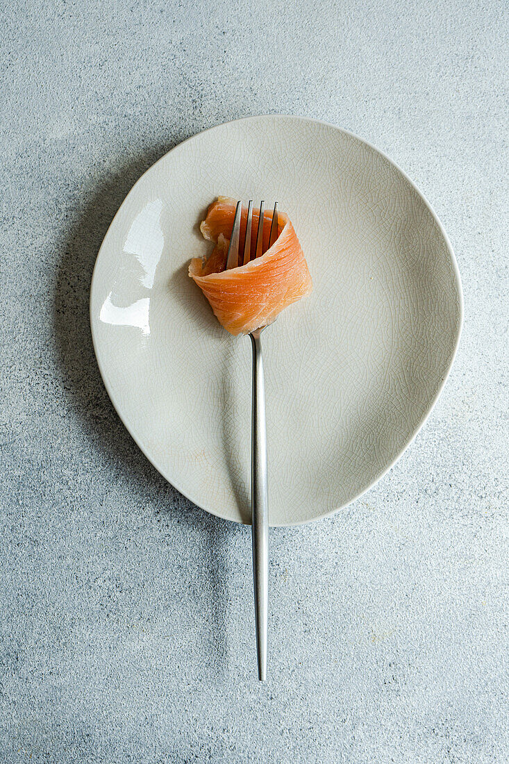 Top view of healthy salmon rolled on fork served on white plate against gray surface