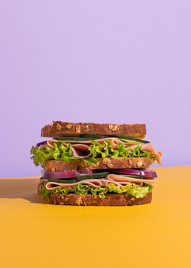 Leckeres Sandwich mit Tomaten, Käsescheiben und frischem Gemüse auf buntem Hintergrund