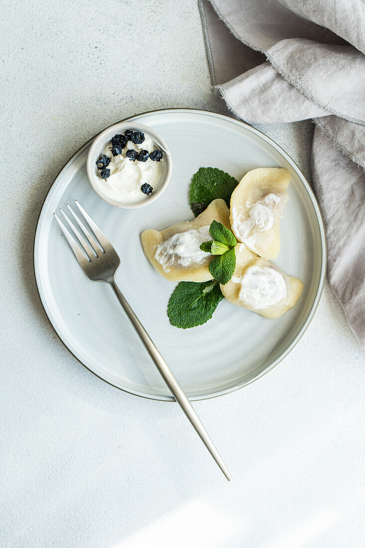 Top view of a tasty traditional Ukrainian dumplings with cherry and sour cream with mint