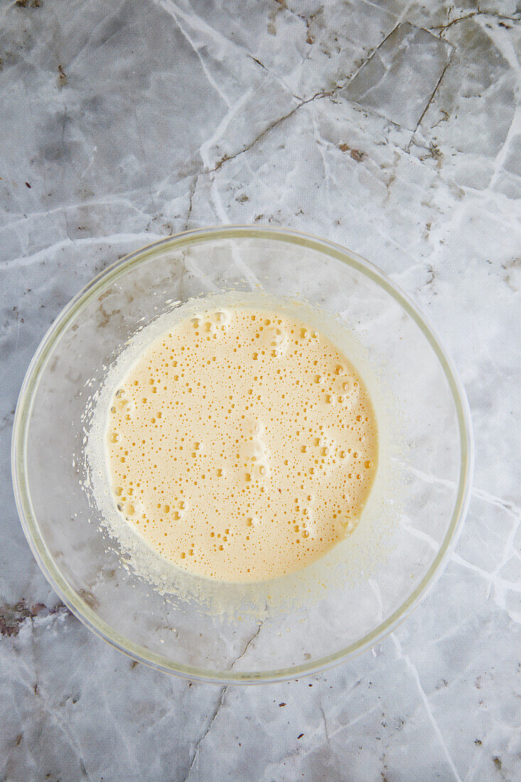 Top view of beaten egg whites in bowl placed on marble table during pastry cooking