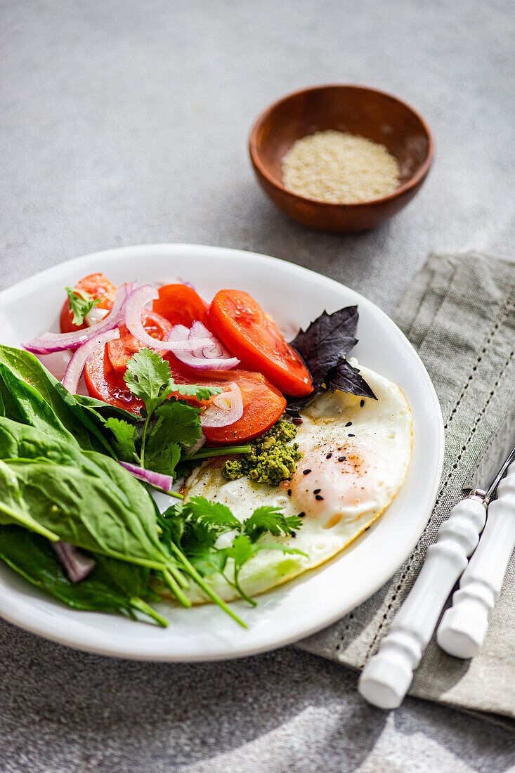 Frisches Keto-Frühstück mit pochierten Eiern, Spinat, Tomaten und Kräutern auf einem weißen Teller, ideal für eine kohlenhydratarme Ernährung