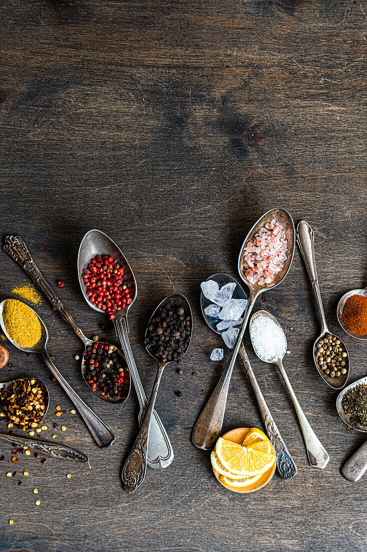 Top view of variety of colorful spices and seeds neatly arranged in spoons on a rustic wooden background for culinary concepts.