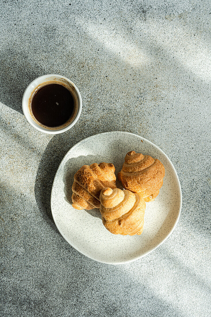 Draufsicht auf einen schwarzen Kaffee und frisch gebackene Croissants auf einem Betontisch