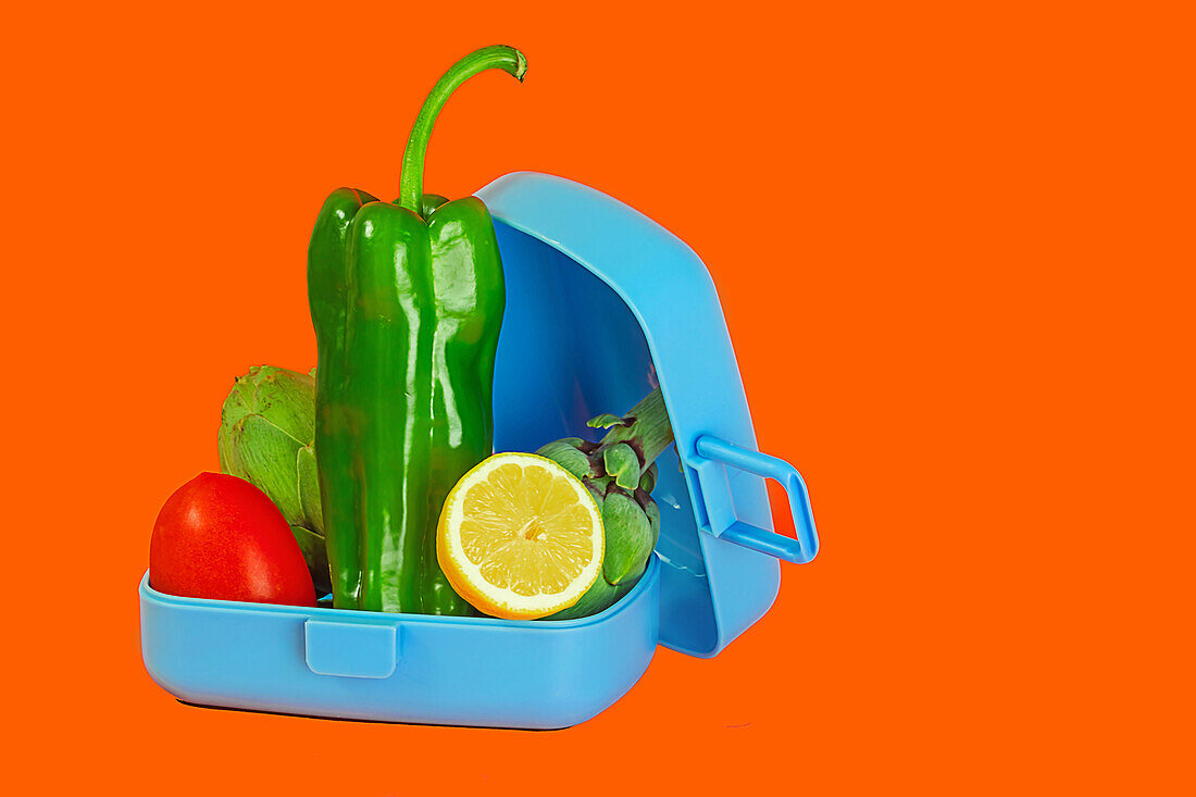 A blue lunch box filled with vibrant green bell pepper, red tomato, and a slice of lime on a contrasting orange background.