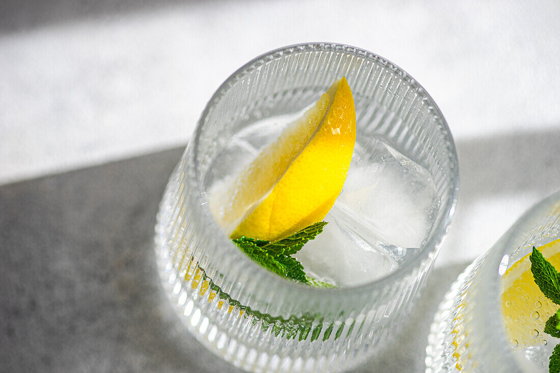 Close-up view of a crystal-clear gin tonic garnished with a fresh lemon slice and ice, perfect for summer refreshments.