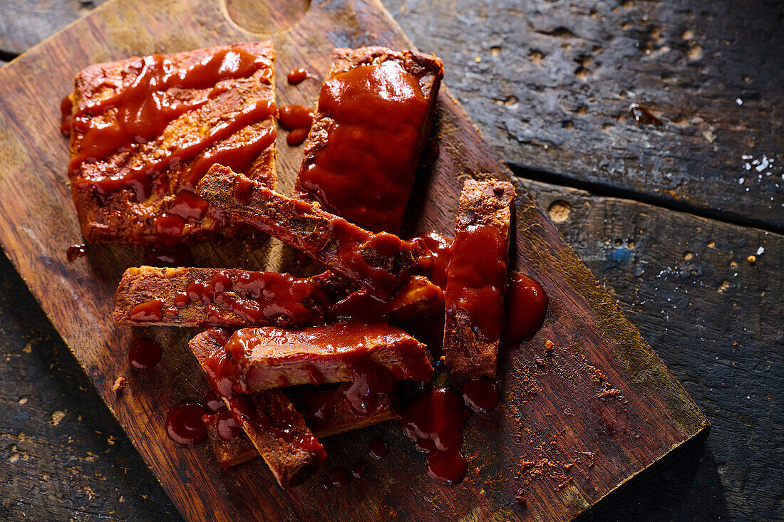 Top view of appetizing grilled pork ribs with ketchup served on wooden board in kitchen