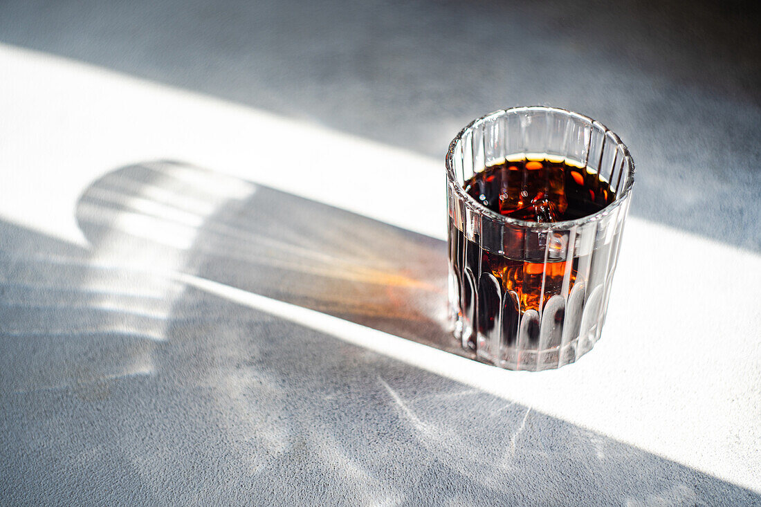 Top view of sunlight filtering through a faceted glass of cherry liqueur casting a sharp shadow on a grey surface
