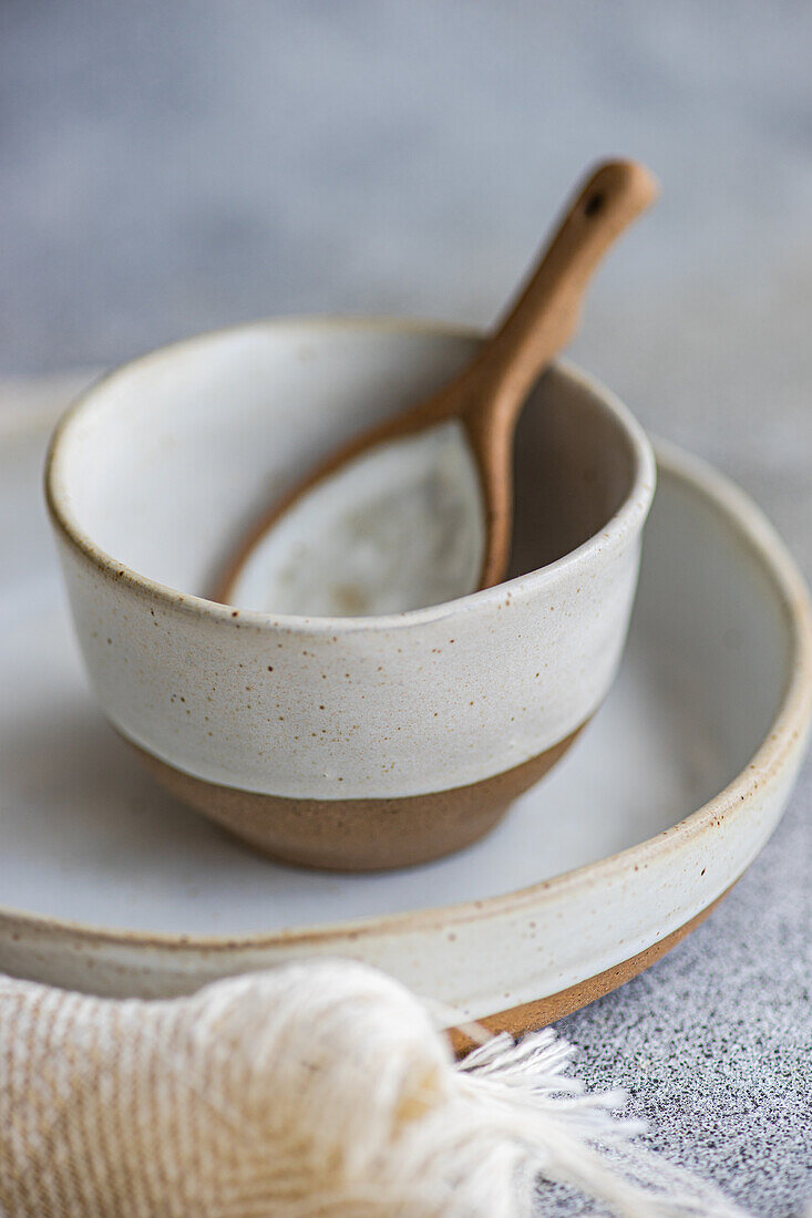 High angle of ceramic tableware set consisting of bowl and plate with wooden spoon placed near napkin on gray surface against blurred background