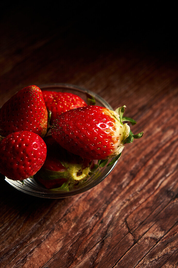 Delicious fresh strawberries with green leaves placed in transparent bowl on wooden table