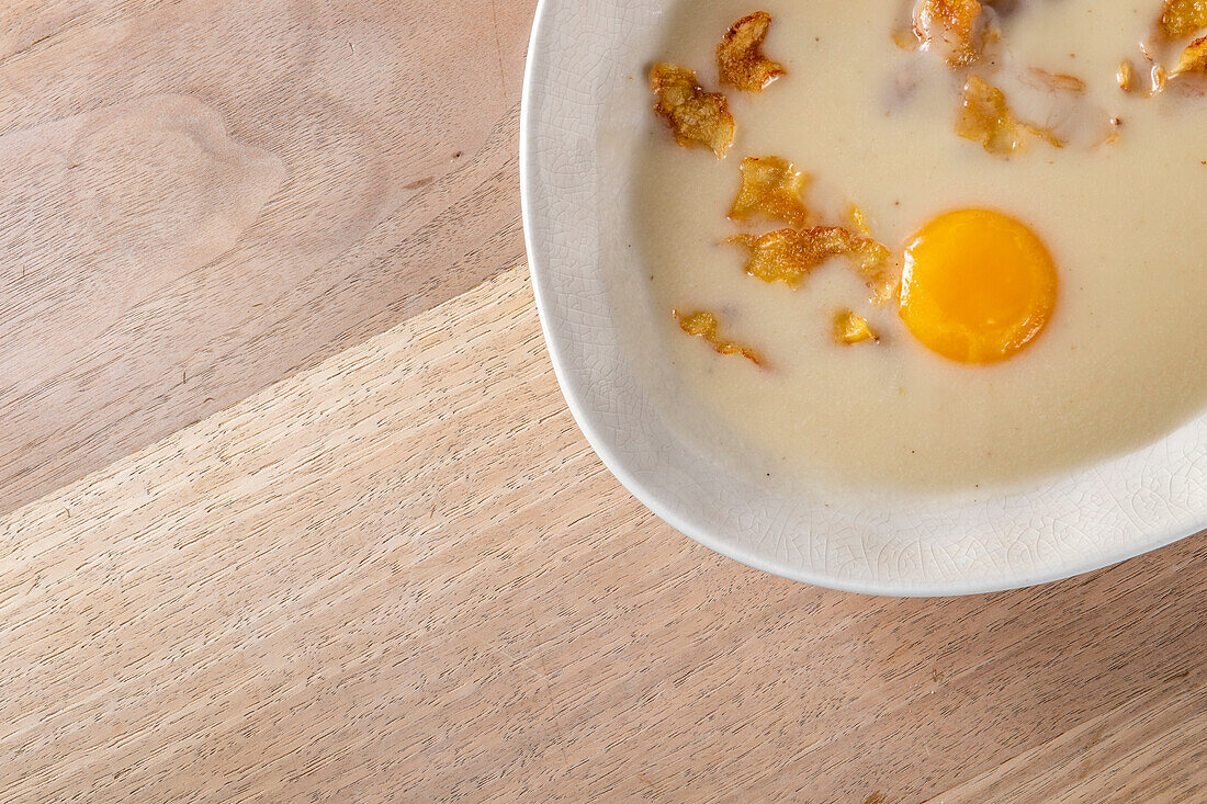 From above creamy sauce with fried strips and raw egg yolk in plate on wooden table