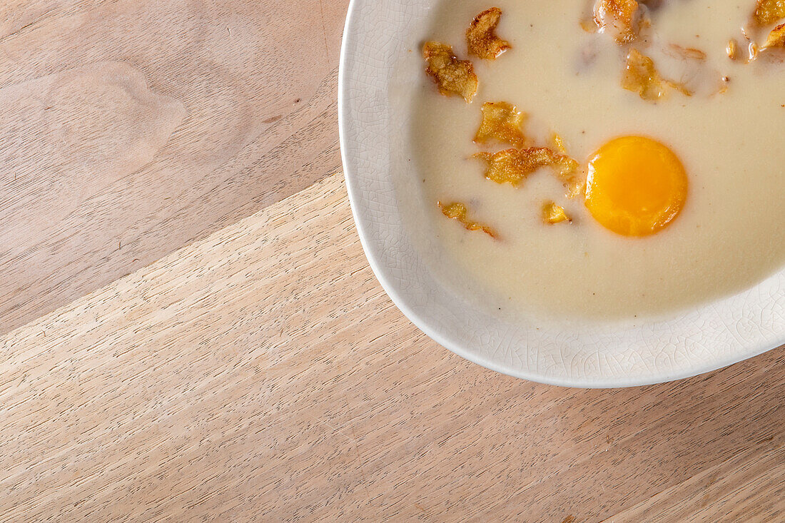 Von oben cremige Sauce mit gebratenen Streifen und rohem Eigelb in einem Teller auf einem Holztisch