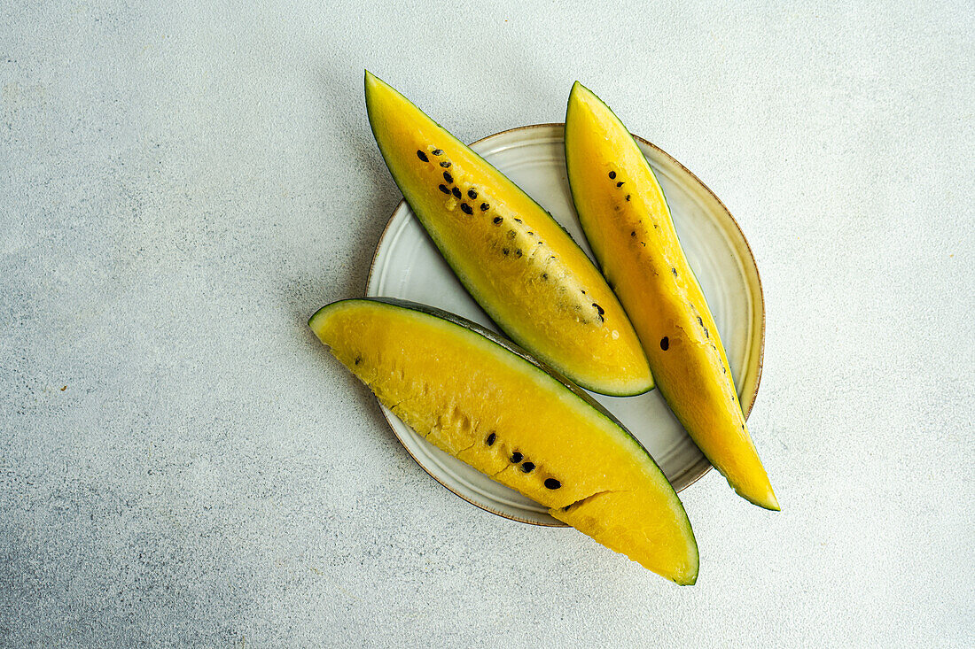 Draufsicht auf Scheiben von gelber Bio-Wassermelone, serviert auf einem Keramikteller vor einer grauen Fläche