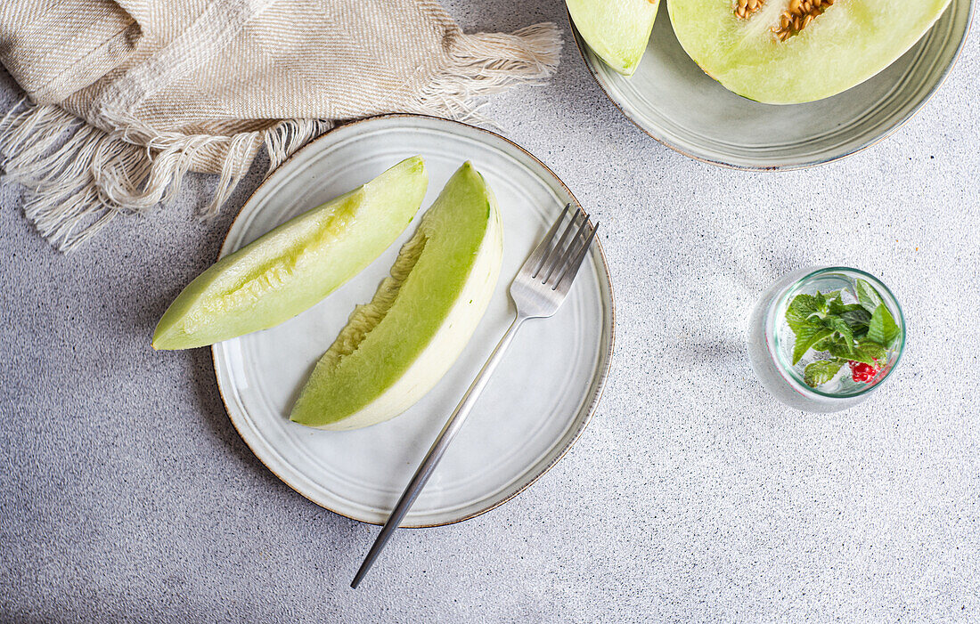 Von oben Scheiben von grüner Melone in einer Keramikschale mit einer Limonade auf Beton Hintergrund platziert