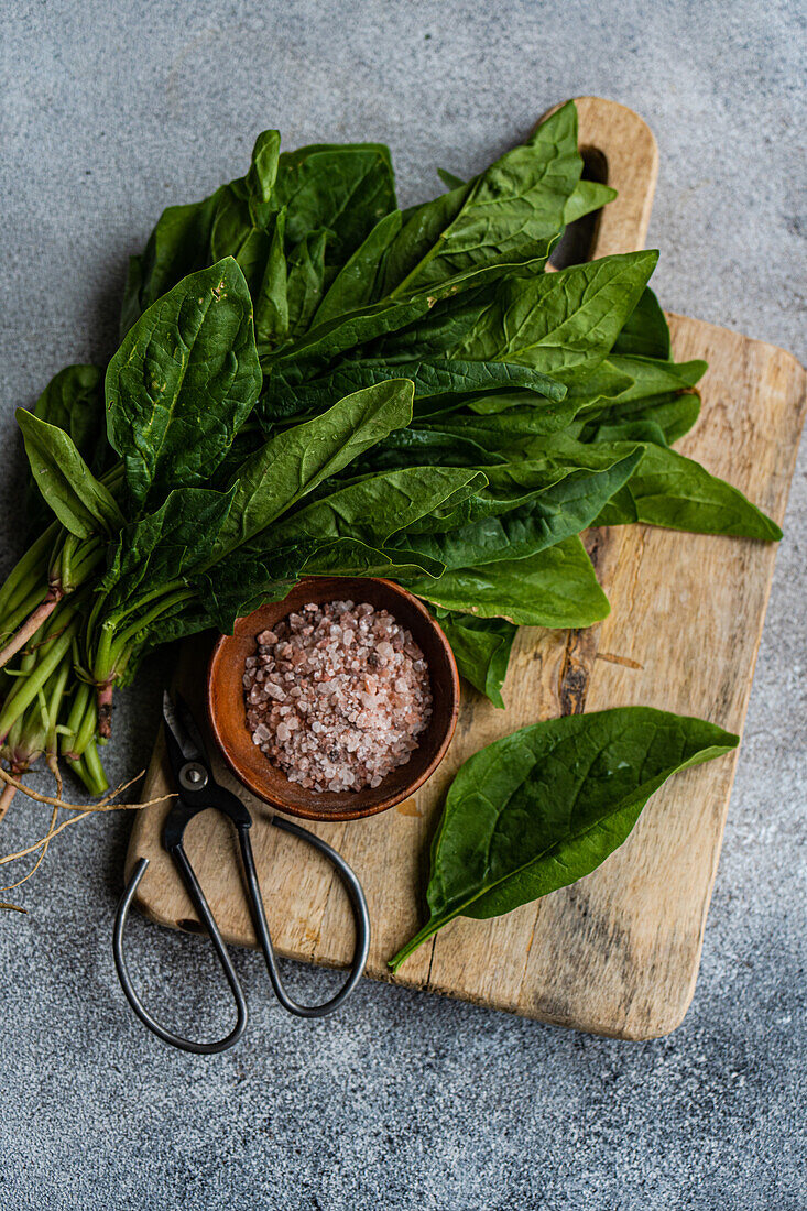 Top view of bunch of fresh spinach leaves on rustic wooden board accompanied by aromatic spices in bowl symbolizing healthy salad preparation