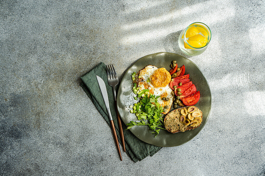 Top view of plate with delicious healthy lunch including fried eggs with tomatoes slices, parsley, spring onion, capers served with glass of cold pure water and lemon slices