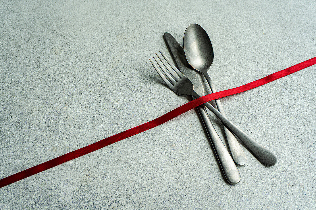 High angle of vintage cutlery set placed on gray surface with red ribbon in light kitchen