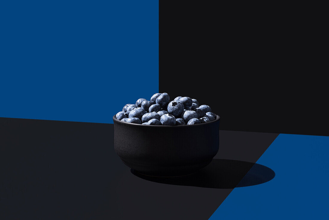 Eine minimalistische Komposition mit einer schwarzen Schale Blaubeeren auf einem geteilten blauen und schwarzen Hintergrund mit dramatischer Beleuchtung