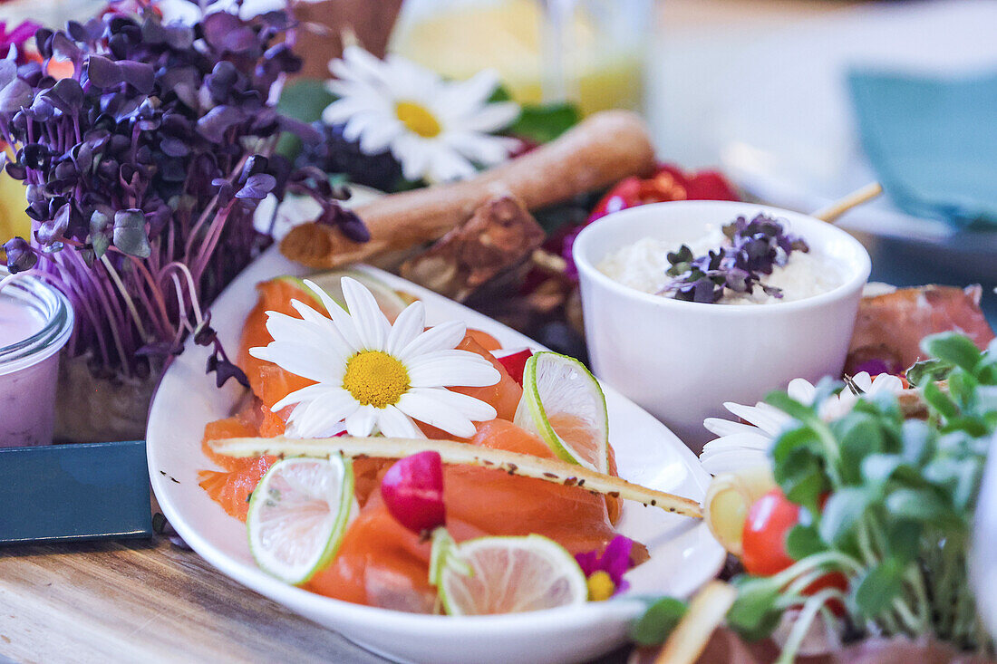 A colorful gourmet brunch spread featuring smoked salmon, edible flowers, fresh vegetables, dip, and citrus slices.
