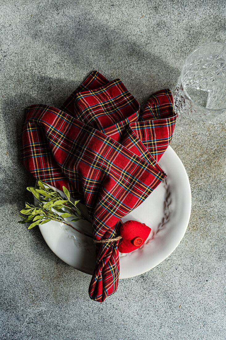 Top view of ceramic plate with cutlery, tartan fabric napkin with heart shaped decor placed on concrete surface at kitchen table for meal during Valentine's day celebration