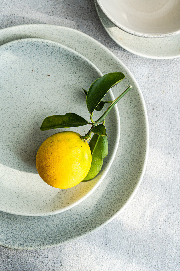 Eine einzelne reife Zitrone mit Blättern auf einem strukturierten Keramikteller, der Einfachheit und organische Schönheit zeigt