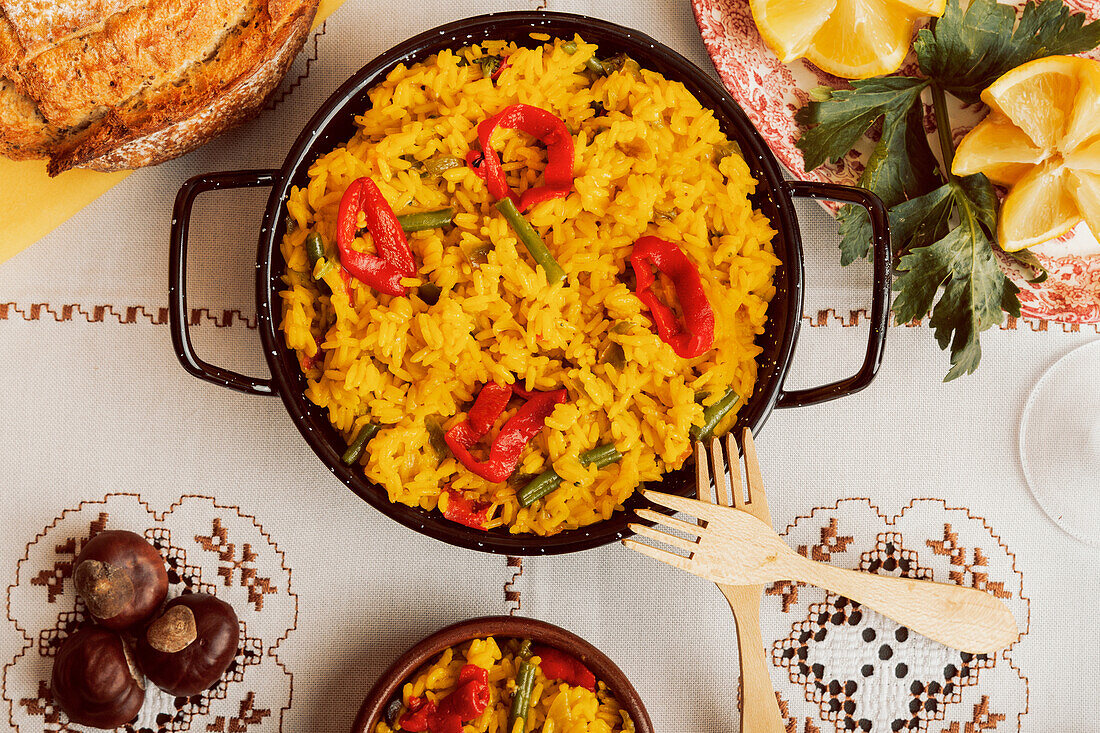 Paella served in traditional pan with lemon and tomato garnish, surrounded by various dishes.