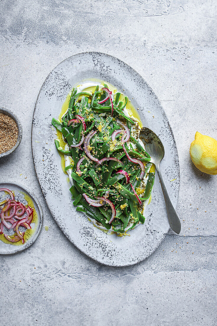 Draufsicht auf einen appetitlichen vegetarischen Salat mit grünen Kräutern und Zwiebelscheiben, der auf einem Teller mit Öl serviert und mit Zitronenschalen garniert wird