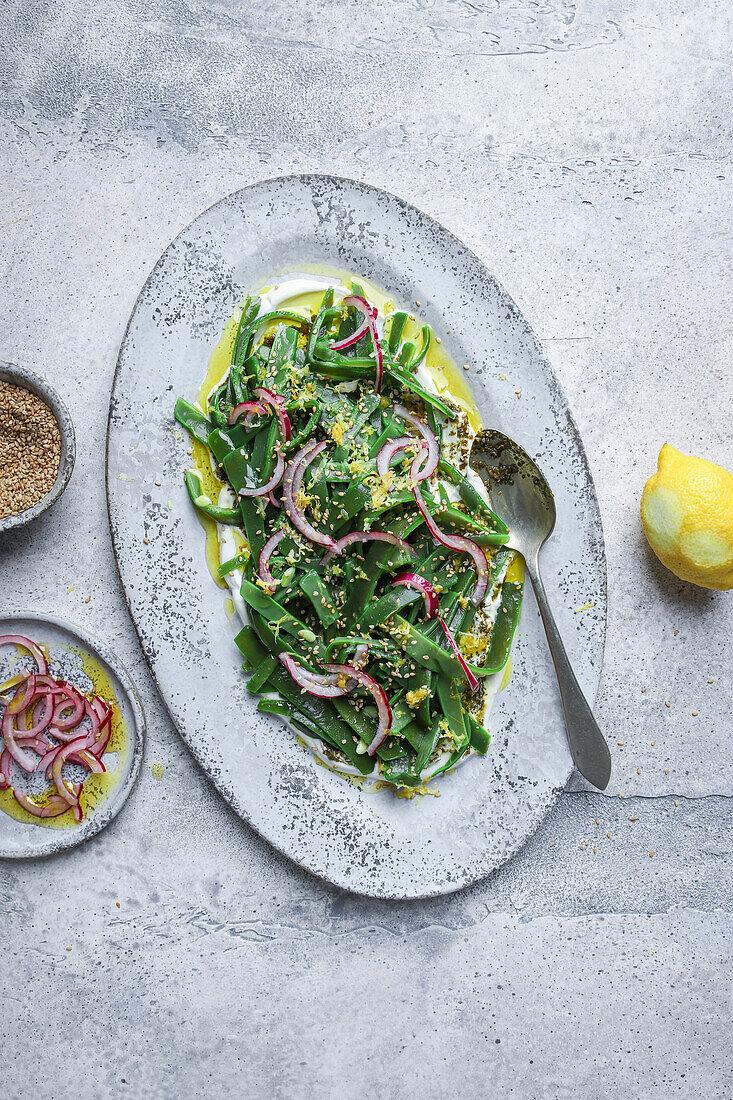 Top view of appetizing vegetarian salad with green herbs and onion slices served on plate with oil and garnished with lemon peel on table